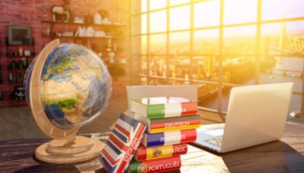 Languages learning and translate, communication and travel concept, books with covers in colors of flags of Europe countries, laptop and globe on a table in a modern interior